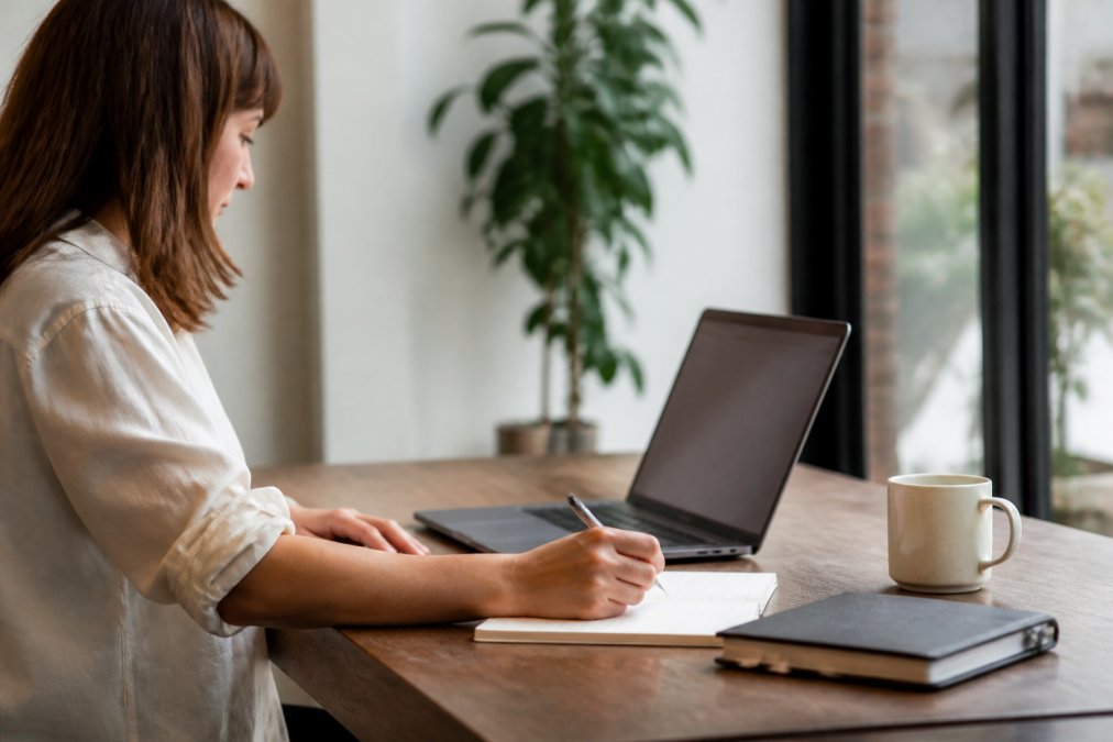 Marketing manager reviewing technical SEO metrics on a laptop screen in a bright office, with notebooks, pen, and coffee cup on the desk beside her