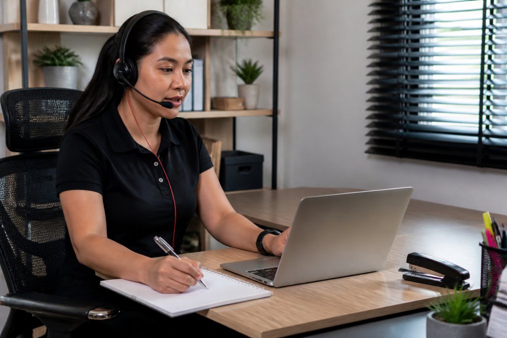 Virtual staff member in professional home office environment with ergonomic desk setup, multiple monitors displaying customer management and dispatch software, actively managing customer communications and service scheduling