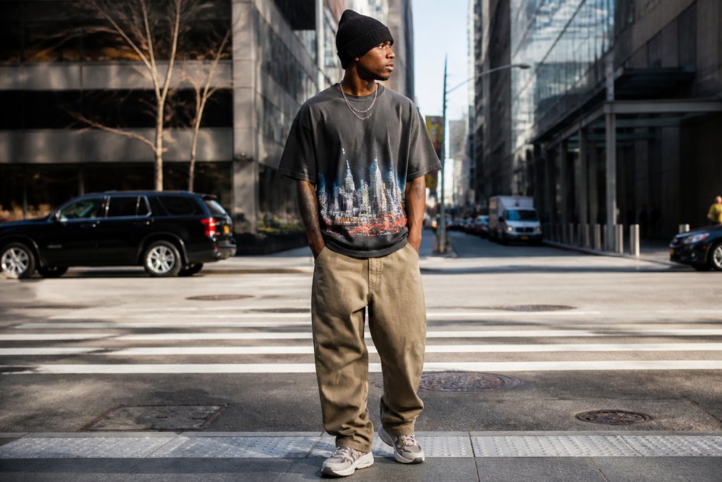 Urban tastemaker styled in traditional streetwear with boxy oversized tee featuring city graphic, relaxed silhouette, and heritage-inspired pieces standing in metropolitan street setting with natural sunlight