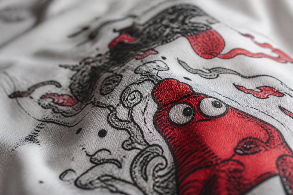 Close-up of hand-drawn graphic design on high-quality t-shirt fabric, showing intricate line work and vibrant ink detail with natural lighting highlighting texture
