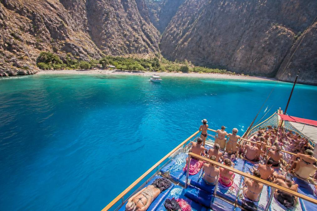 Türkoise renkli su ve kıyıdaki yüksek kayalıklarla çevrili Kelebekler Vadisi'nin hava görünüşü, teknede eğlenen ve güneşlenen turistler ön planda