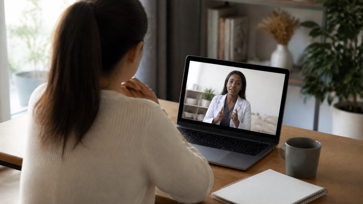 Professional sitting at home at a desk with a laptop during a video call with a healthcare provider, showing a calm, comfortable telehealth environment