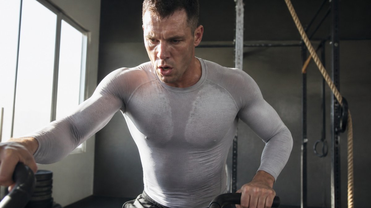 Athlete wearing lightweight baselayer during intense CrossFit workout, showing sweat dispersal and fabric fit in action with natural gym lighting