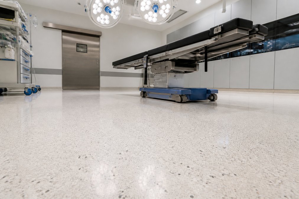 Close-up of seamless terrazzo flooring in a modern hospital operating room showing the smooth, continuous surface with subtle aggregate patterns and professional lighting highlighting the uniform finish