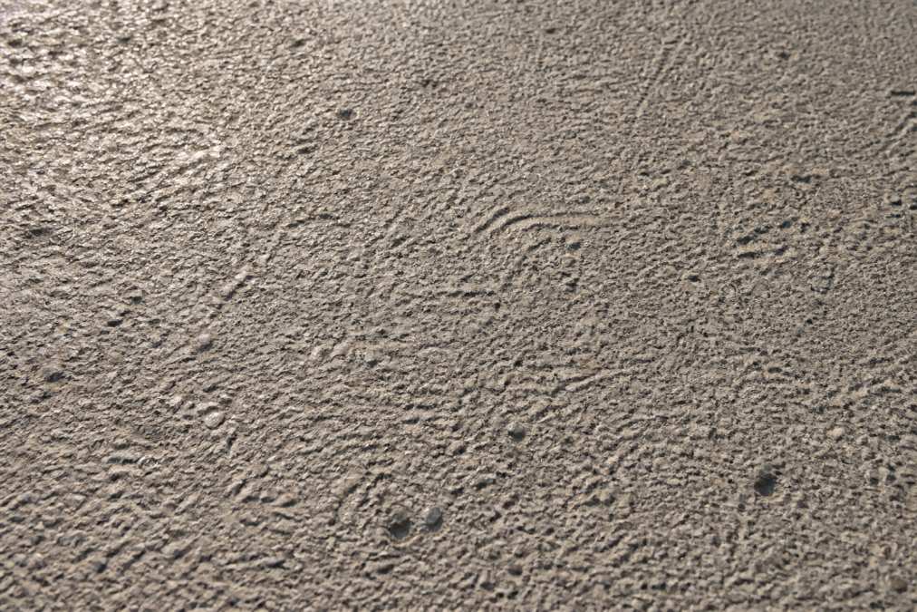 Close-up of concrete floor showing exposed aggregate texture and surface profile from shotblasting, with light highlighting the roughness and mechanical tooth of the prepared substrate