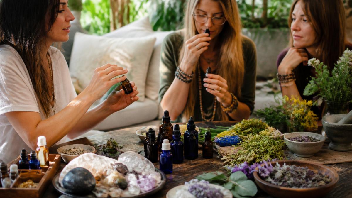 Assortment of essential oil bottles in amber and cobalt glass with fresh botanicals, crystals, and dried herbs arranged on a wooden surface in warm natural sunlight