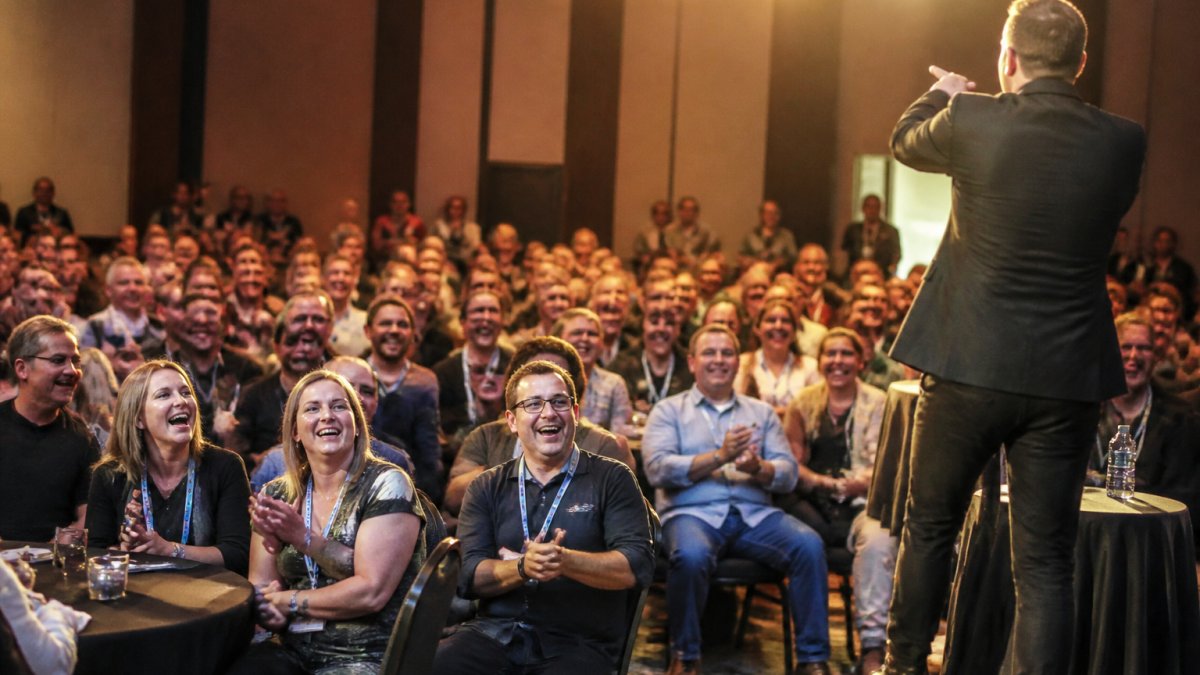 A packed audience applauds a performer during a high energy corporate entertainment event on stage.