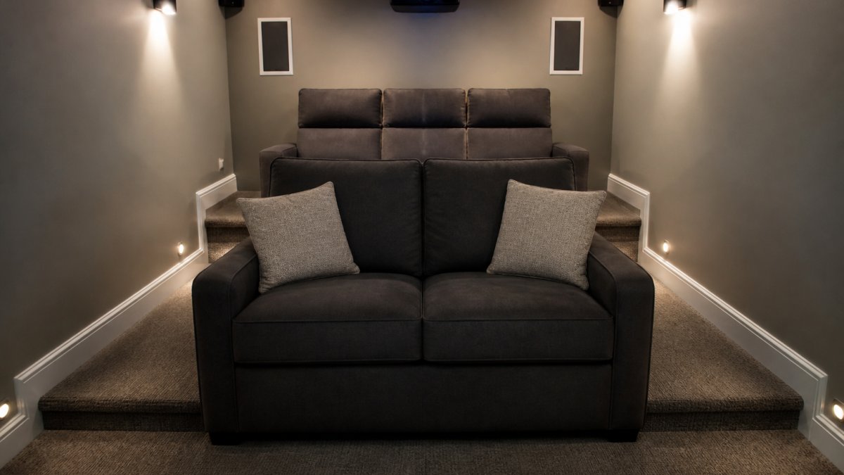 Cozy small media room with a loveseat positioned against the wall, compact footprint with clear walkway space visible on both sides, neutral lighting showing tiered arrangement