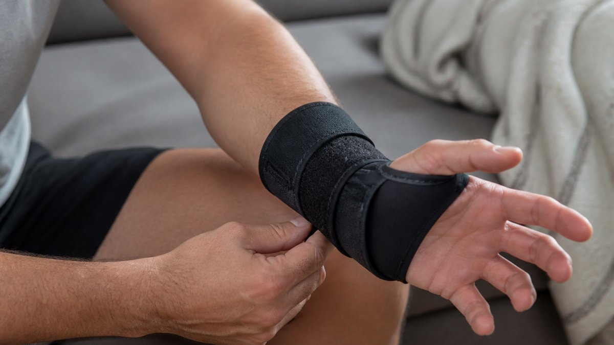 Close-up of a person's wrist wearing a premium cold compression sleeve during a recovery session, showing the sleeve's fit and neoprene material quality