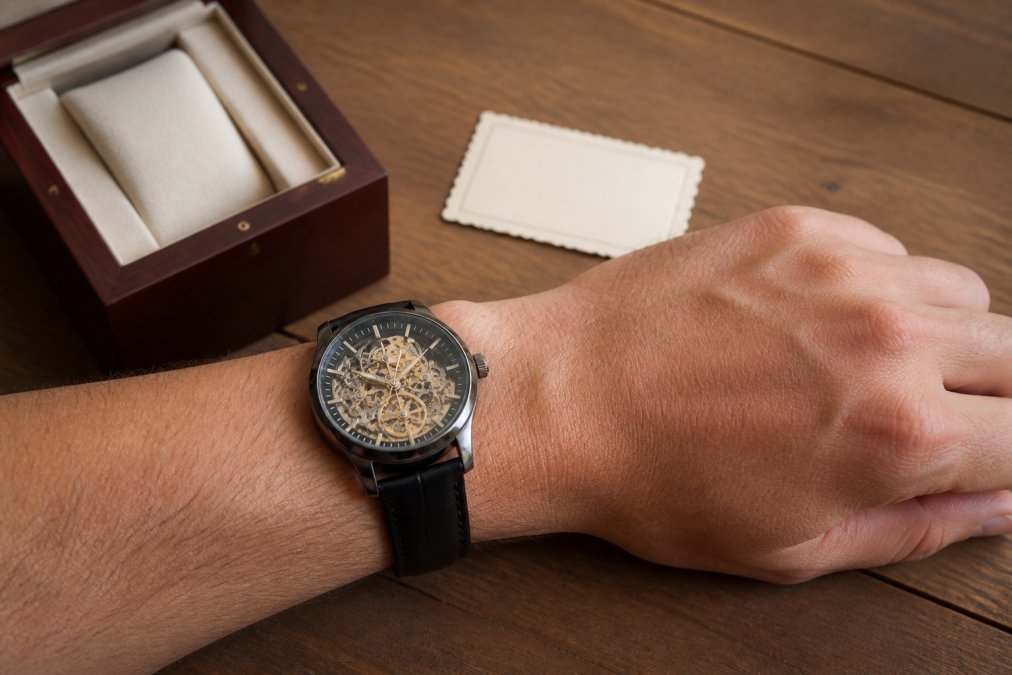 Engraving process for fossil watches shown with a leather skeleton watch and gift box on a wooden table