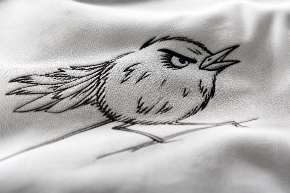 Close-up of premium cotton fabric texture with hand-drawn graphic design visible, showing fine weave detail and print durability with natural studio lighting