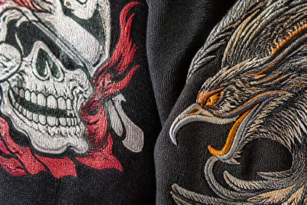 Close-up of screen-printed and embroidered graphic designs on quality heavyweight cotton fabric, showing crisp ink lines and detailed stitching under natural studio lighting