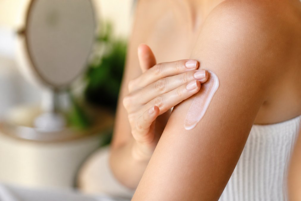 Close-up of hands applying creamy natural body lotion to skin, showing the luxurious texture and smooth absorption on soft skin in warm natural lighting