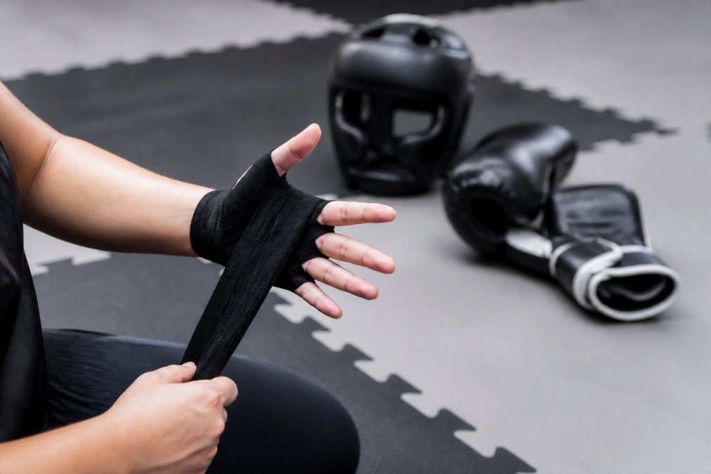 Martial artist wrapping hands for sparring near professional martial arts gear on a gym mat