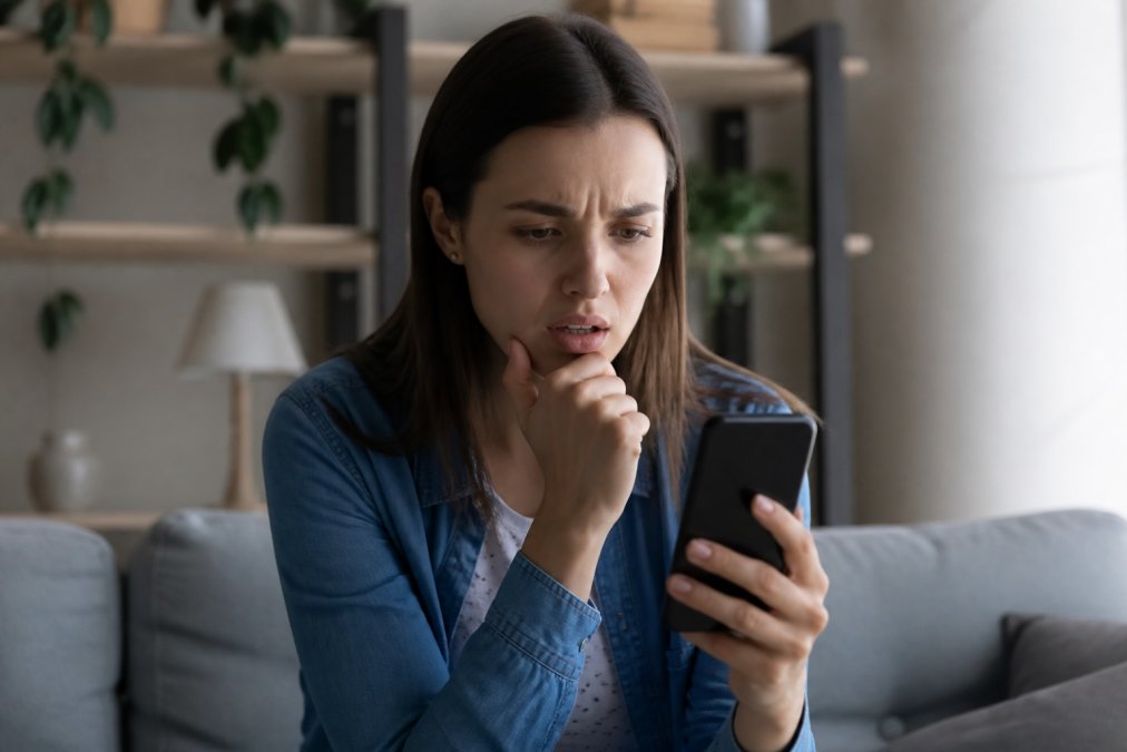 Person holding a smartphone with a warning message displayed, looking concerned at the screen in natural indoor lighting