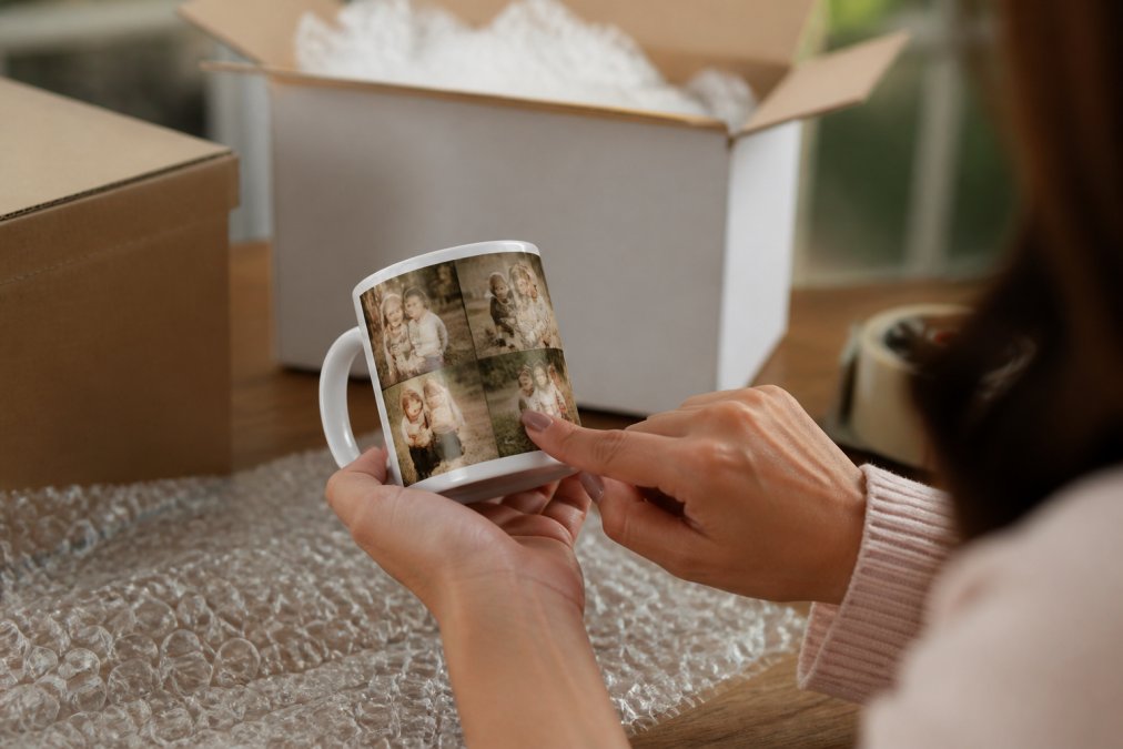 Close-up of hands holding a personalized gift item while reviewing a digital proof on a smartphone screen, with the product displayed on a wooden table in natural window lighting