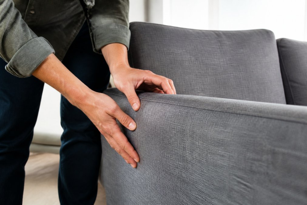 Close-up of hands carefully examining upholstery seams and fabric texture on a delivered sofa, checking for pulls, tears, or manufacturing defects in natural afternoon light