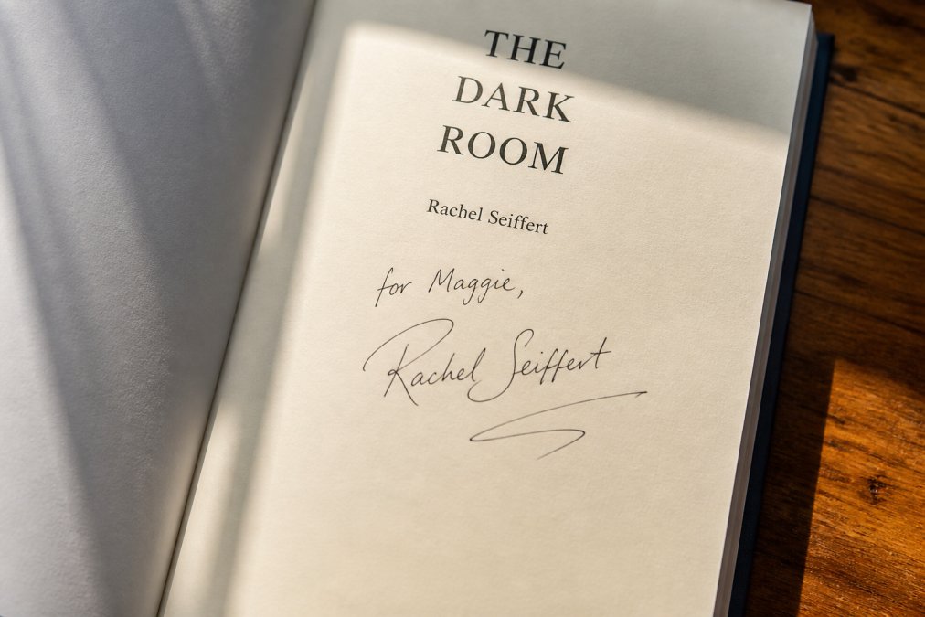 Close-up of an open signed book showing the author's signature on the title page, with natural lighting highlighting the pen markings and page condition
