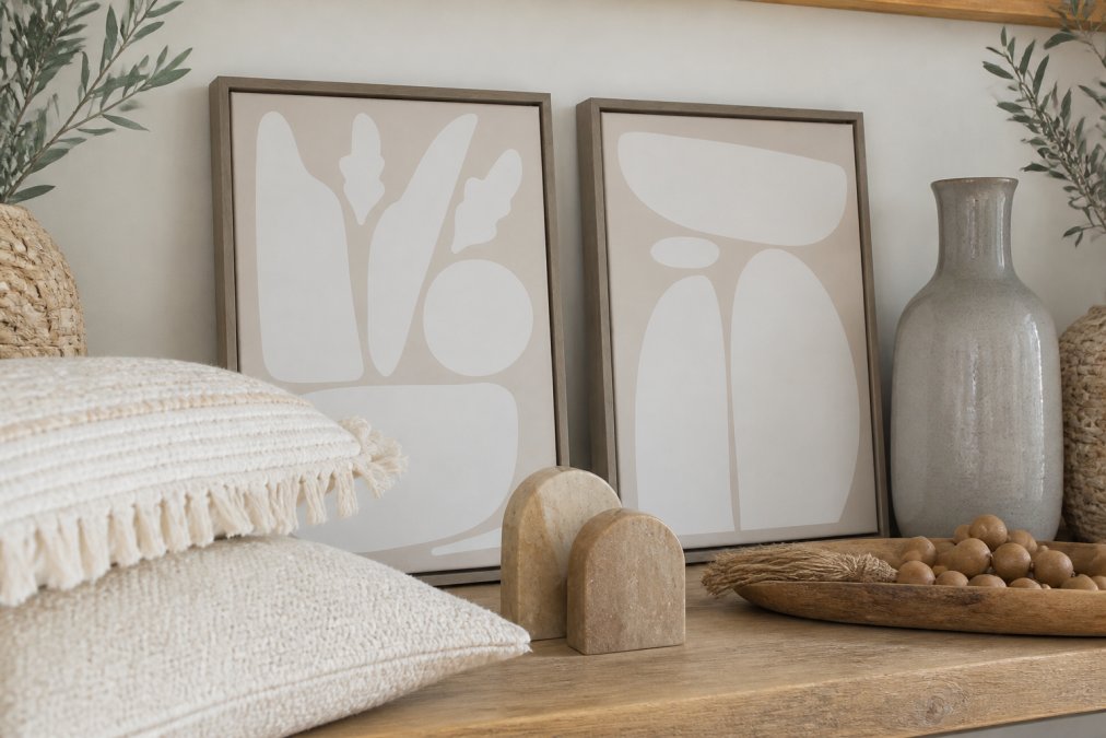Close-up of layered home decor on a shelf featuring woven throw pillows in cream, ceramic vase in soft gray, stone bookends, and natural wood accents arranged together, showing varied textures and materials