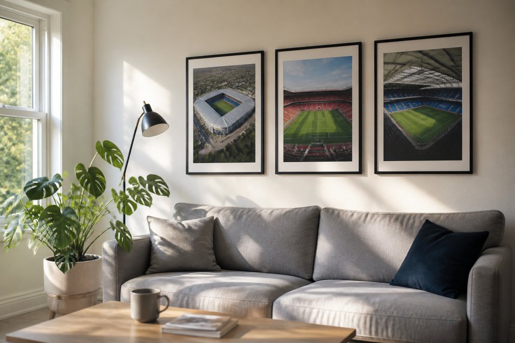 A bright living room wall with three framed football stadium prints hung in a neat row above a grey sofa, a plant and a floor lamp nearby, warm afternoon light coming through a window