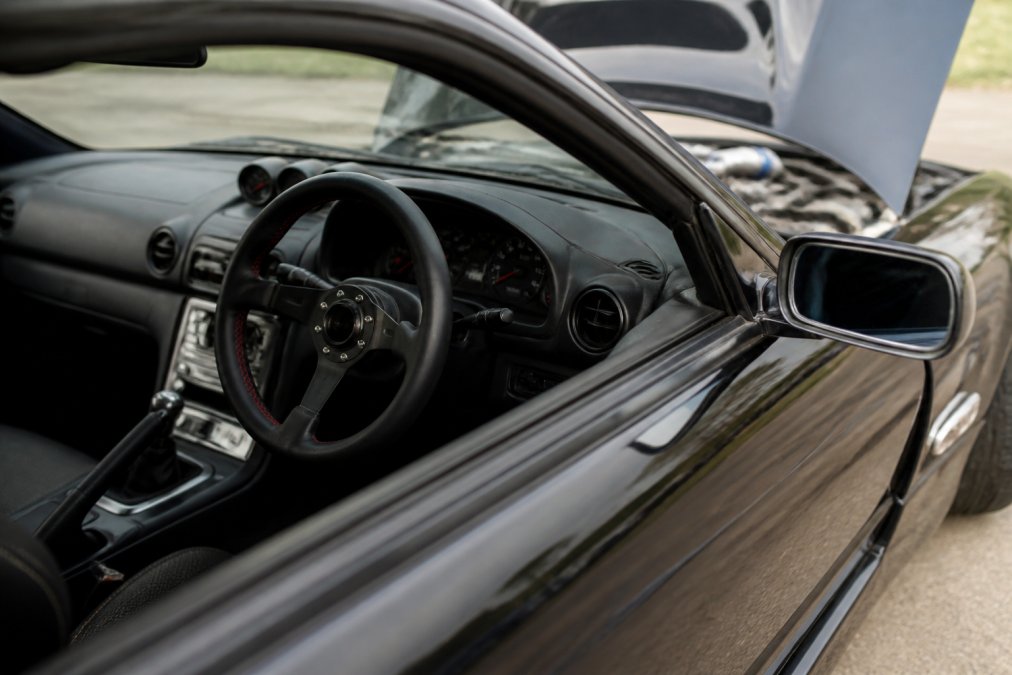 Close-up of a smartphone screen displaying a detailed classified listing for a modified car with high-quality photos of the engine bay, suspension, and interior customization details