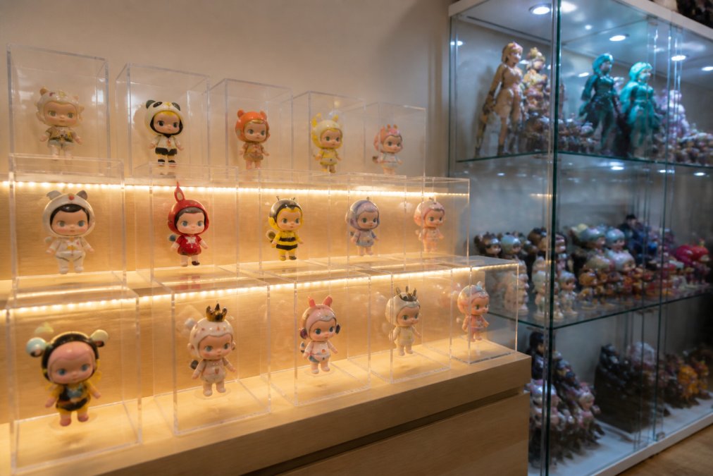 Collectible vinyl figures from blind box collecting displayed on tiered acrylic risers inside a glass cabinet.