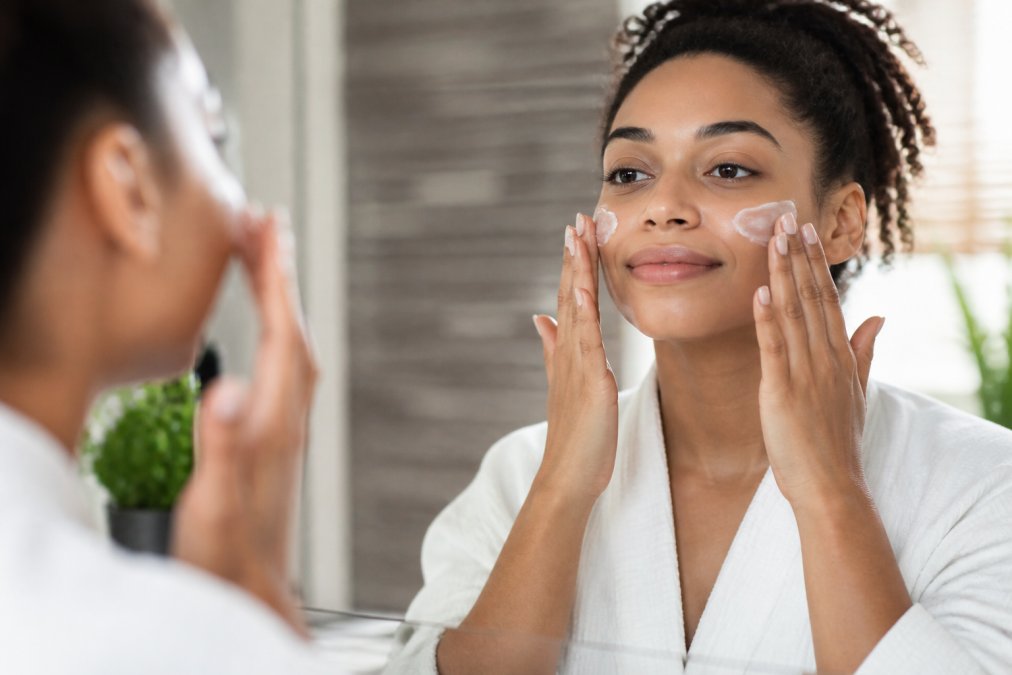 Close-up of hands gently applying luxurious botanical skincare product to the face, with soft natural light highlighting the skin's texture and radiance