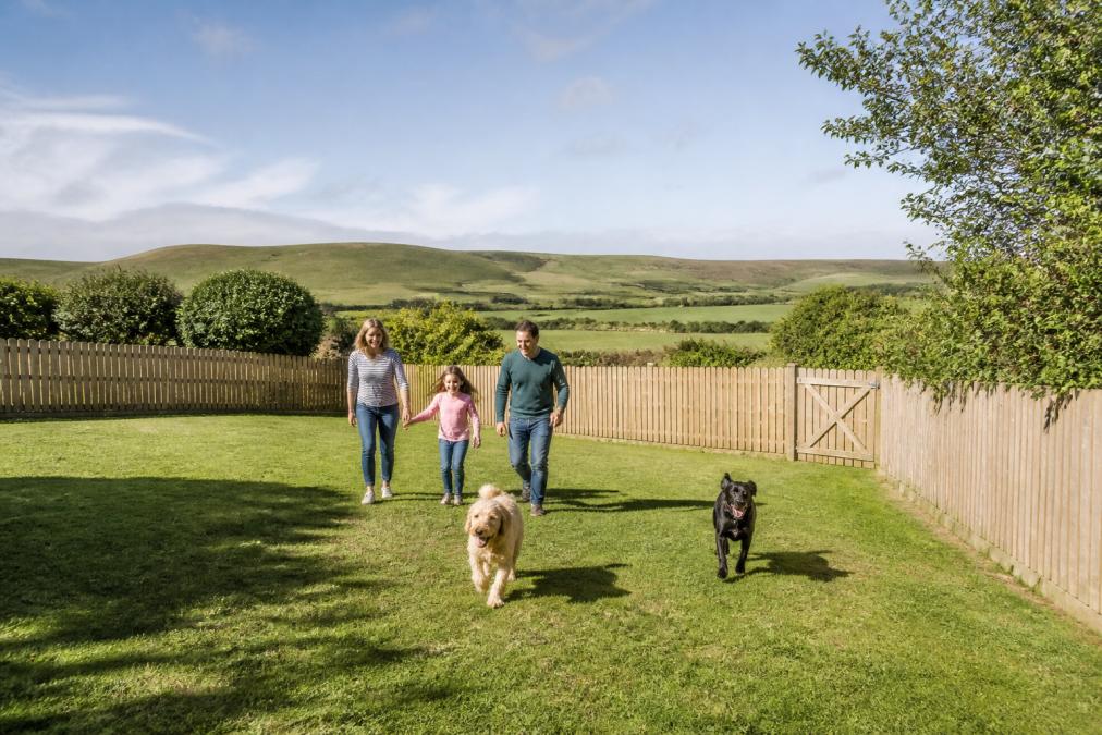 Spacious enclosed garden with secure fencing, family with two dogs enjoying the outdoor space, countryside views and rolling hills visible in the background