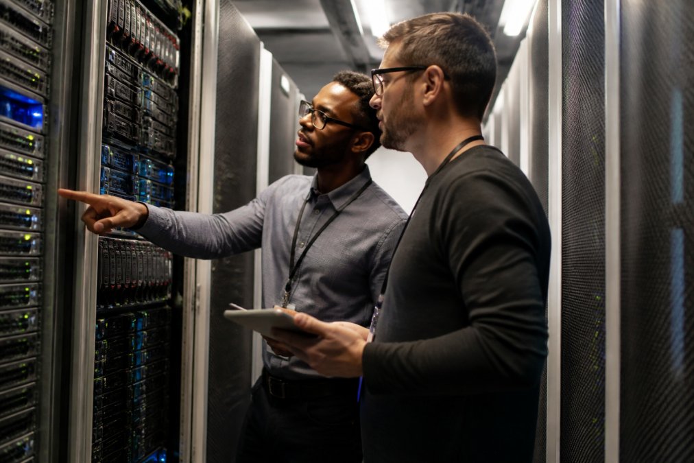 IT technicians monitoring multiple screens in a secure operations center with network displays, cybersecurity dashboards, and real-time alerts glowing across dark monitor banks