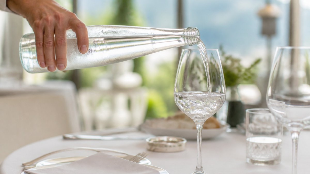 An elegant table setting with a chilled glass bottle of mineral water being poured into a wine glass, soft natural light, fine dining atmosphere