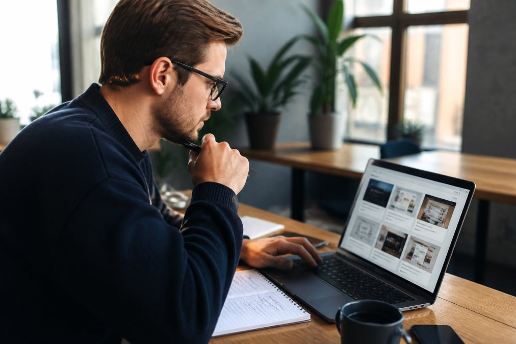 Professioneel aan een bureau werkend op laptop met notitieblok en koffie, verschillende website-opties vergelijkend op het scherm