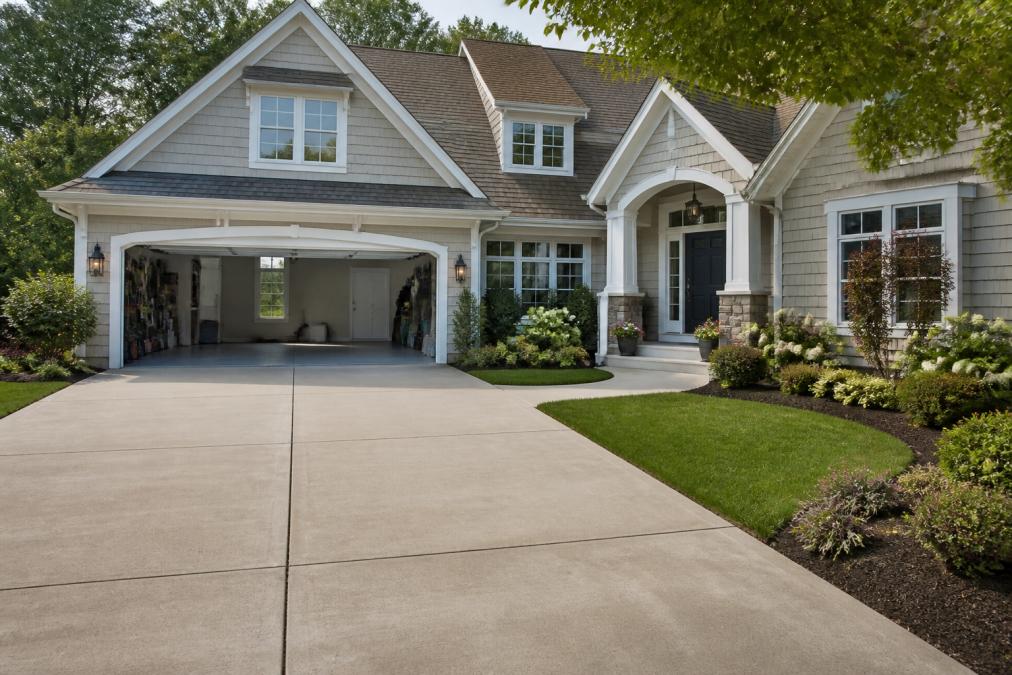 A well-maintained home exterior with a clean, clear driveway, open garage showing organized space, fresh landscaping, and a welcoming front entrance ready for showing