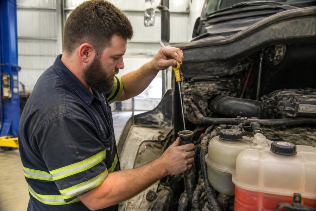 Mechanic checking diesel truck engine oil level and inspecting fluid reservoirs under bonnet during routine maintenance in workshop