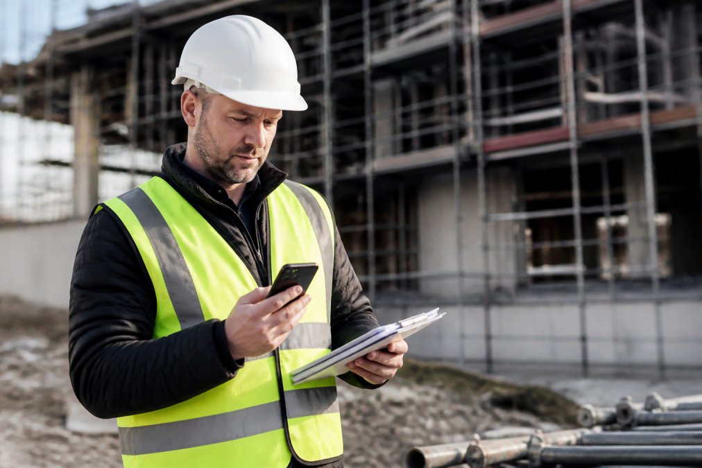 Construction supervisor reviewing field notes tools on a smartphone at an active job site with scaffolding