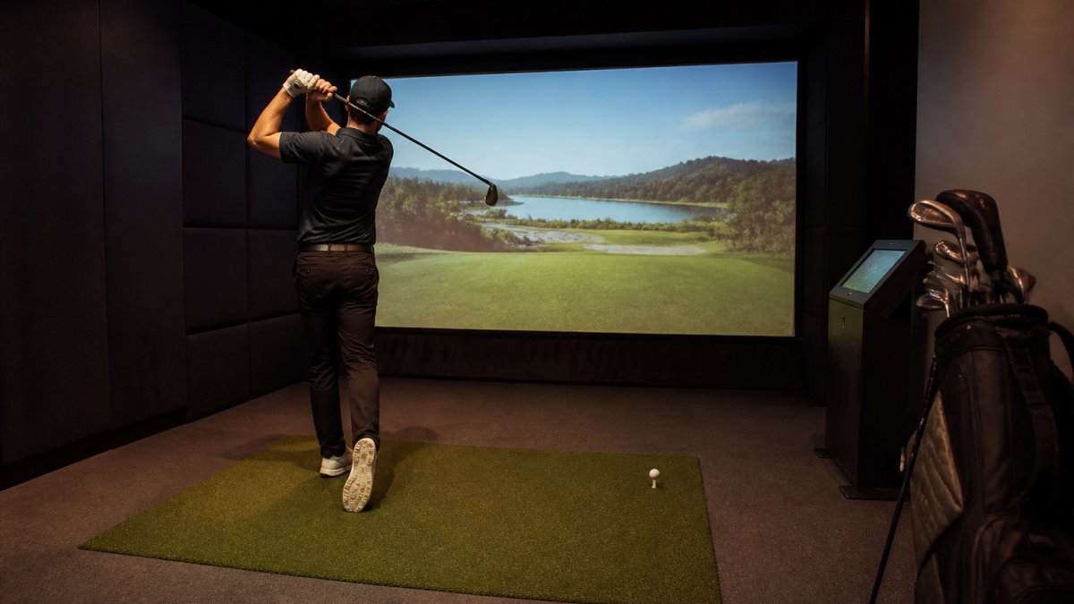 A golfer mid-swing inside a modern indoor simulator bay, large projection screen showing a famous golf course, dim ambient lighting, realistic turf mat underfoot
