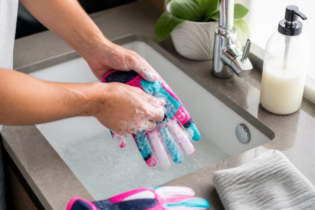 Close-up of hands gently washing a pair of colorful batting gloves in a sink with mild soap and water, soft lighting, clean background