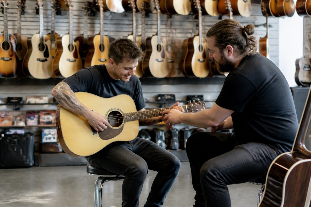 A bright, modern music shop interior in Robina, Gold Coast, with guitars hanging on the wall and a staff member helping a customer try an acoustic guitar
