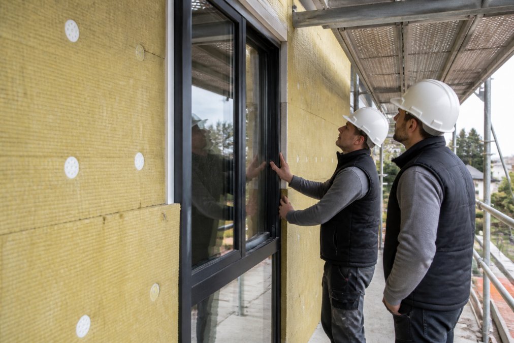 Close-up van moderne isolatiematerialen en energiezuinige ramen die in een gevelrenovatie worden geïnstalleerd, met werkmannen die de afwerking controleren in daglicht