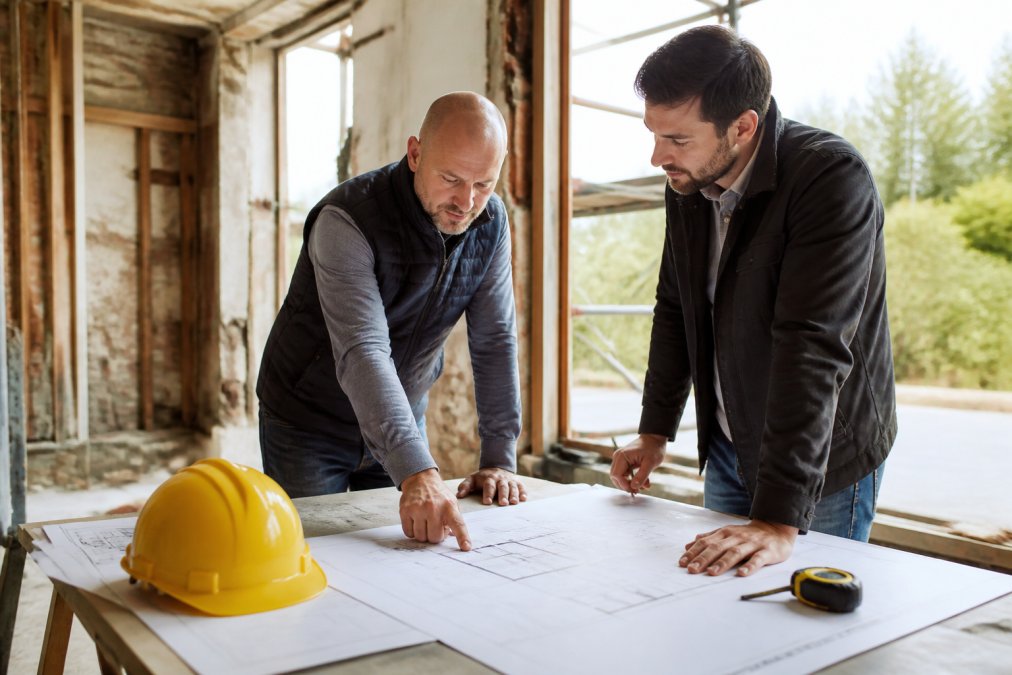 Architect en aannemer bespreken bouwtekeningen bij een totaalrenovatie met of zonder architect in een oude woning.