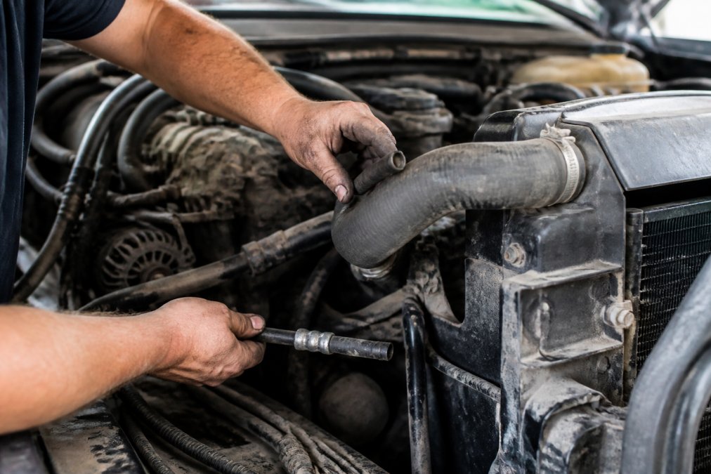 Close-up of mechanic's hands inspecting transmission cooler lines and radiator hoses in older truck engine bay during pre-tow maintenance check