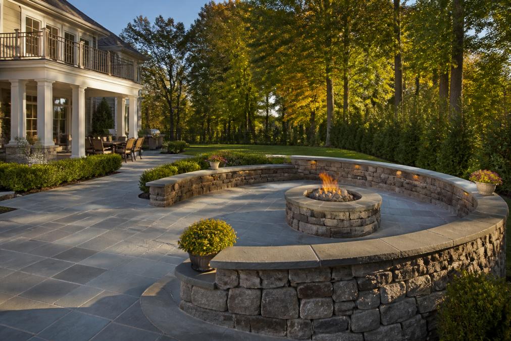 Bluestone patio with a stone retaining wall and fire pit in a luxury outdoor space at sunset
