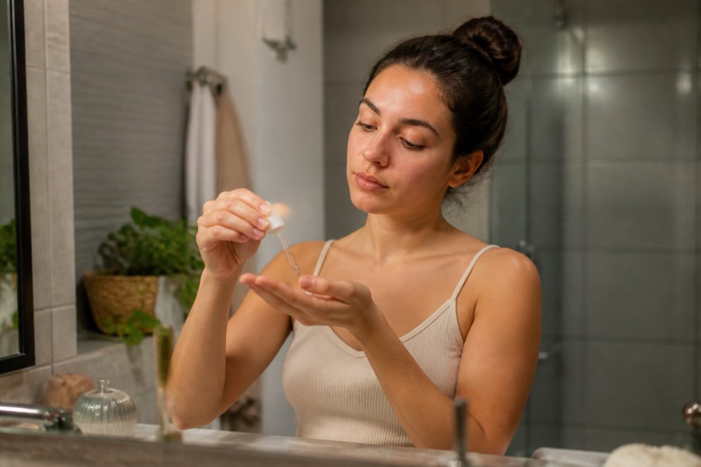 Woman performing evening skincare routine with retinoid serum in modern bathroom with soft lighting