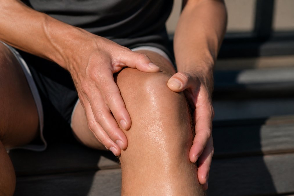 Close-up of hands demonstrating proper application technique of CBD topical freeze gel to the knee area, showing gentle massage motions around the patella and surrounding soft tissue in natural lighting