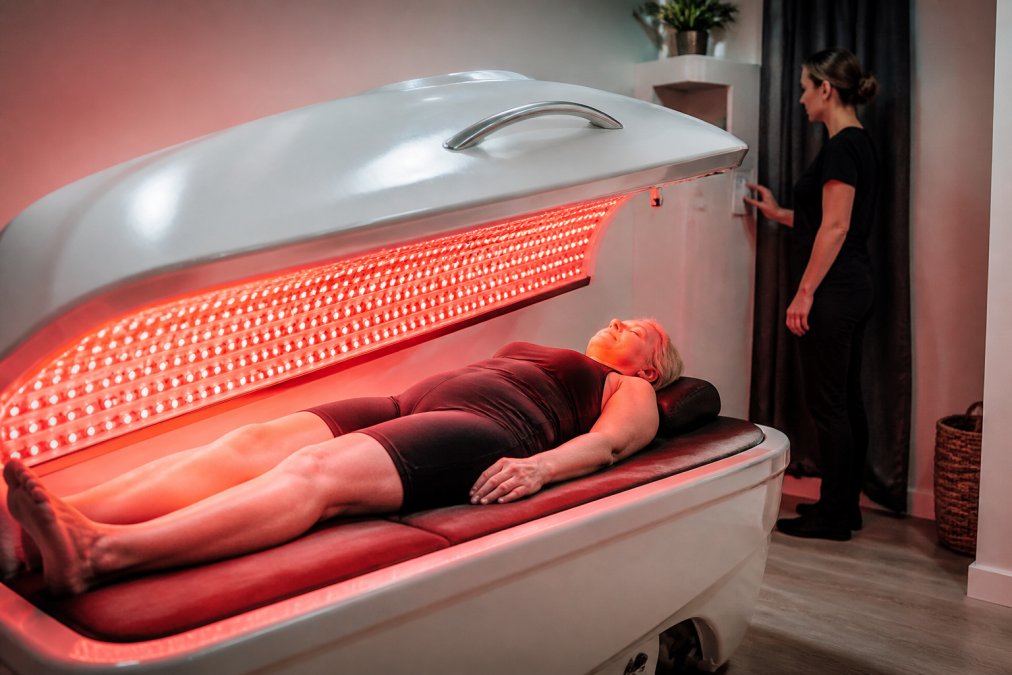 Patient relaxing inside a trifecta red light therapy bed while a clinician adjusts the settings in a modern clinic.