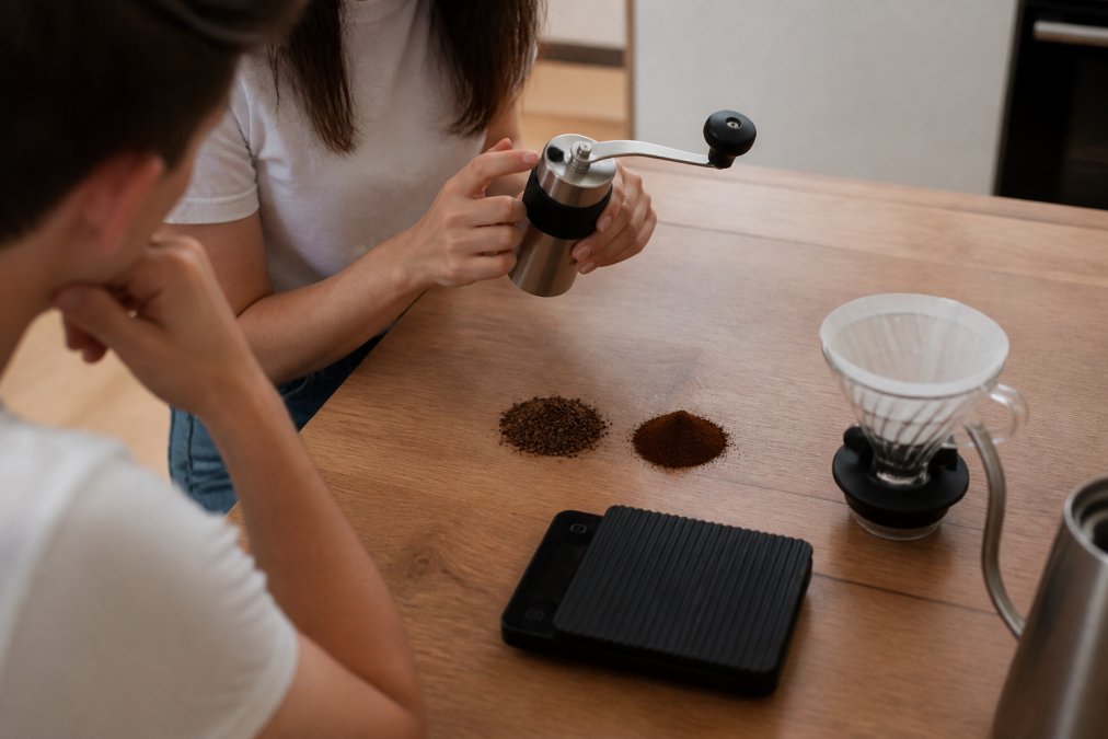 Hand grinder with piles of coarse and fine coffee grounds next to a digital scale and a pour-over dripper
