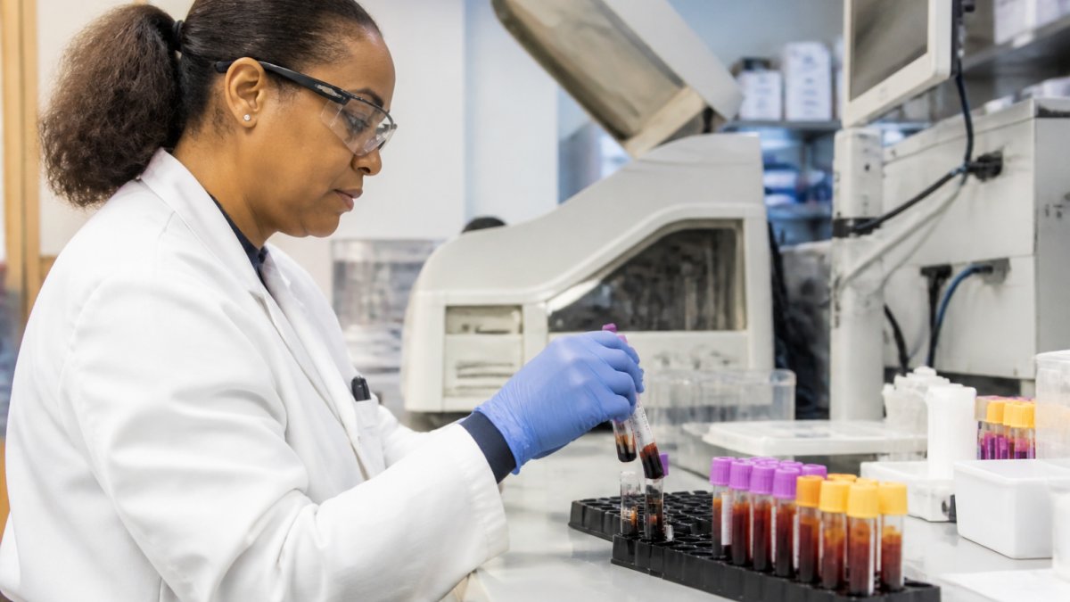 Laboratory technician processing testosterone blood samples in modern clinical lab setting, with test tubes and analyzer equipment visible