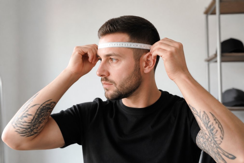 Eine Person misst ihren Kopfumfang mit einem weichen Maßband um den Kopf, auf Augenhöhe und oberhalb der Ohren, wobei die Messung deutlich sichtbar ist