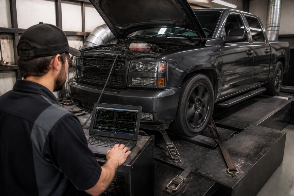 Technician monitoring laptop software while tuning a supercharged pickup truck on a dyno machine