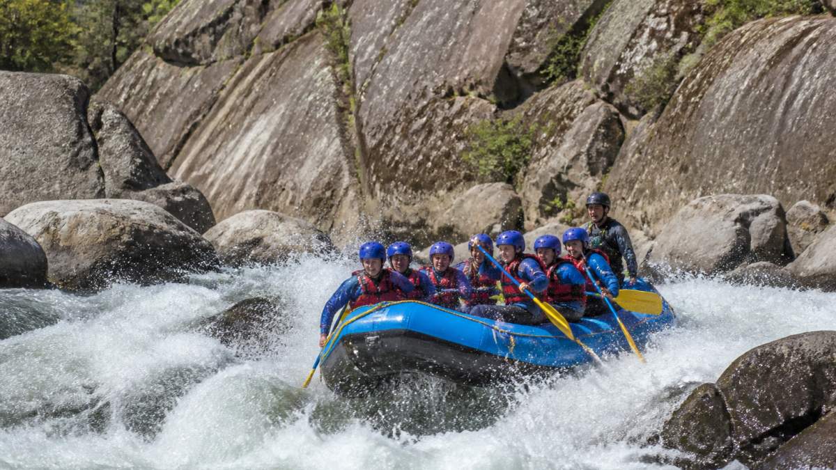 Whitewater guide steering a commercial raft through challenging Tuolumne River rapids under morning sunlight.
