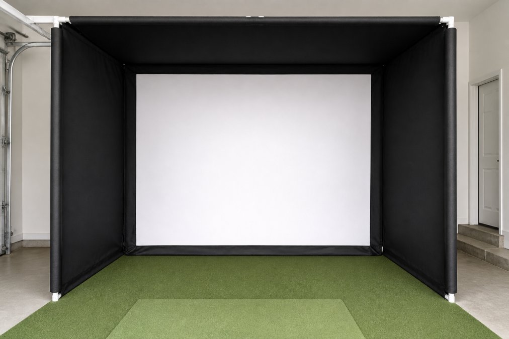 Close-up of a premium golf simulator enclosure frame with black nylon side panels and a bright white impact screen mounted in a clean garage, with foam padding clearly visible on the vertical frame poles and a green artificial turf hitting mat positioned in front
